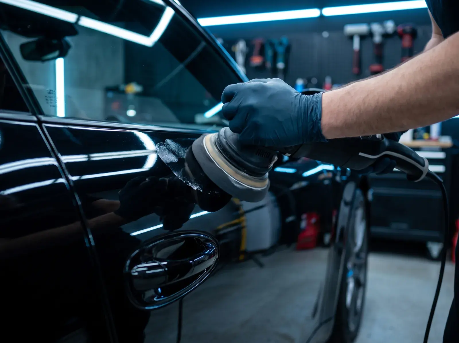 Dual-action polisher removing swirl marks from black Porsche paint during paint correction in St. Louis